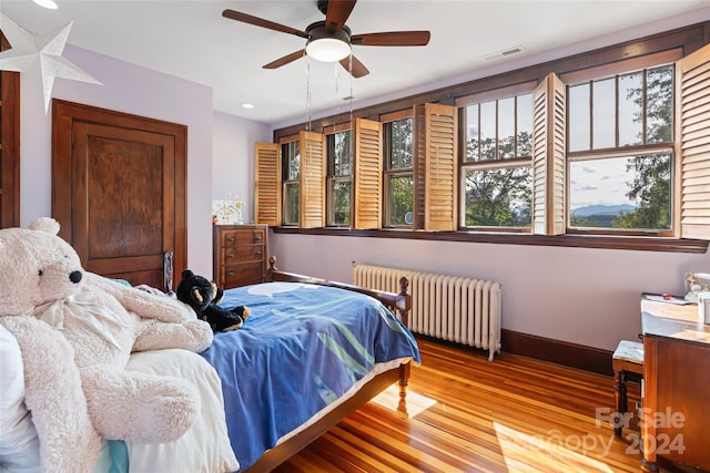 bedroom featuring visible vents, baseboards, ceiling fan, radiator, and wood finished floors
