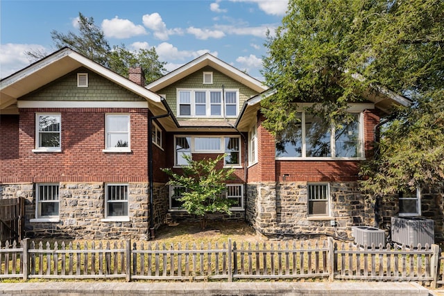 view of front of property with stone siding, a chimney, fence, cooling unit, and brick siding