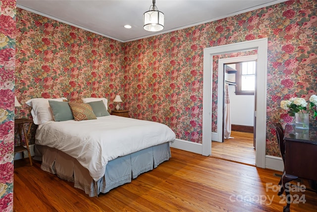 bedroom with baseboards, wood finished floors, and wallpapered walls