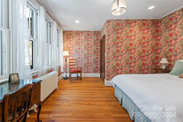 bedroom with radiator heating unit, multiple windows, crown molding, and light hardwood / wood-style flooring