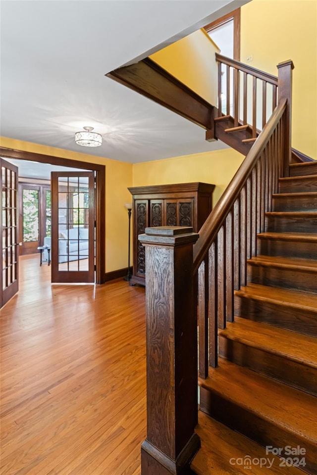 staircase with french doors, wood finished floors, baseboards, and a notable chandelier