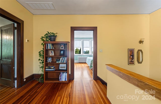 hall with visible vents, baseboards, radiator, and wood finished floors