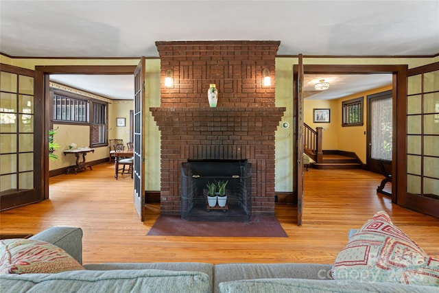 living room featuring ornamental molding, a brick fireplace, stairway, and wood finished floors