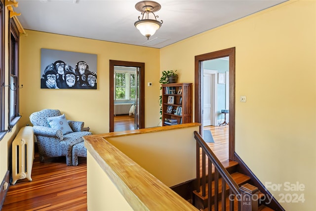 hall with radiator heating unit, an upstairs landing, visible vents, and wood finished floors