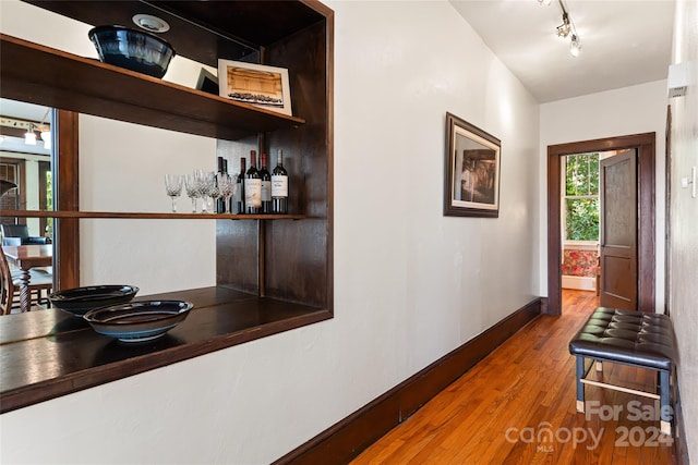 hallway featuring track lighting, wood finished floors, and baseboards