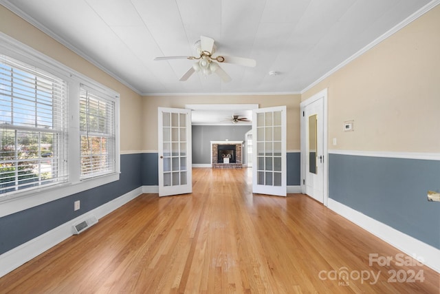 unfurnished living room featuring a fireplace, french doors, light hardwood / wood-style floors, crown molding, and ceiling fan