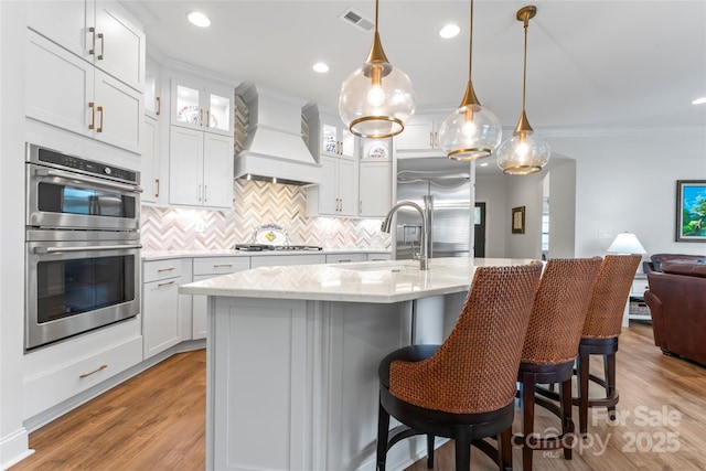 kitchen with an island with sink, stainless steel appliances, sink, and custom exhaust hood