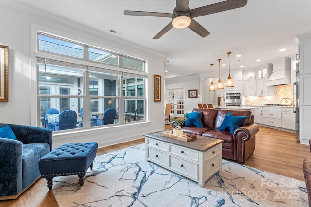 living room with ceiling fan, ornamental molding, and light hardwood / wood-style flooring