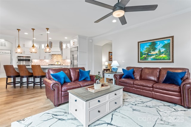 living room featuring ceiling fan, ornamental molding, and light wood-type flooring