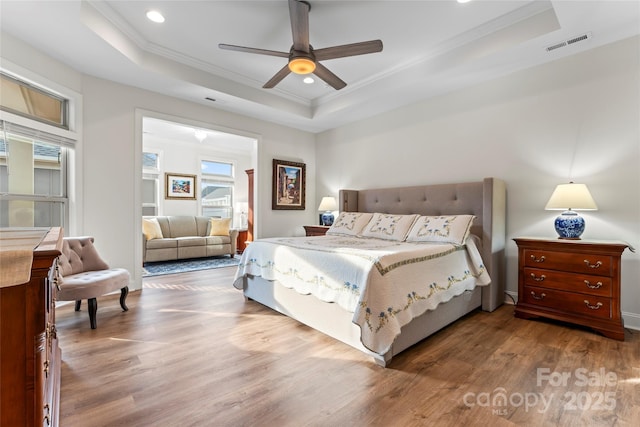 bedroom with wood-type flooring, ornamental molding, a raised ceiling, and ceiling fan