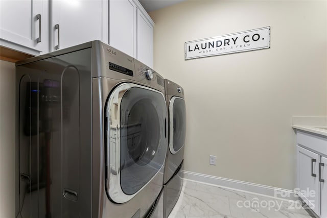 clothes washing area with separate washer and dryer and cabinets