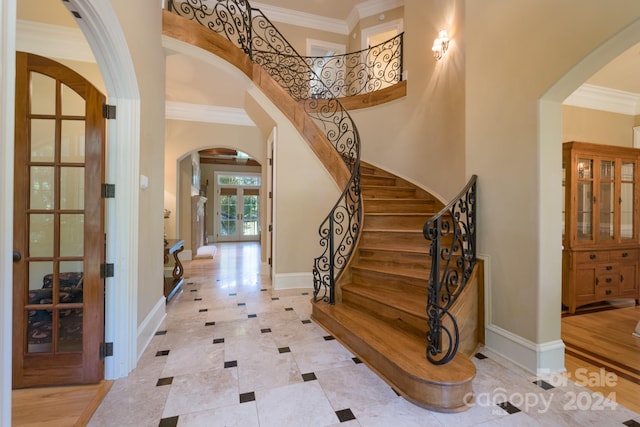 foyer entrance with light wood-type flooring, ornamental molding, and a towering ceiling