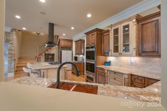 kitchen featuring appliances with stainless steel finishes, light stone counters, a breakfast bar area, exhaust hood, and light wood-type flooring