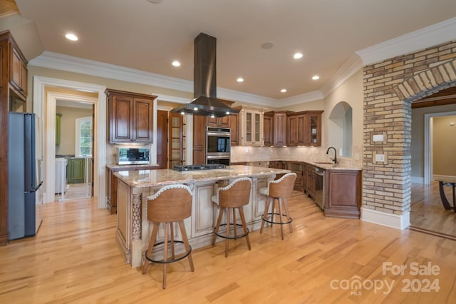 kitchen featuring sink, island range hood, light hardwood / wood-style flooring, decorative backsplash, and appliances with stainless steel finishes