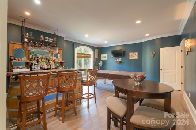 dining room featuring light hardwood / wood-style flooring, ornamental molding, and bar area