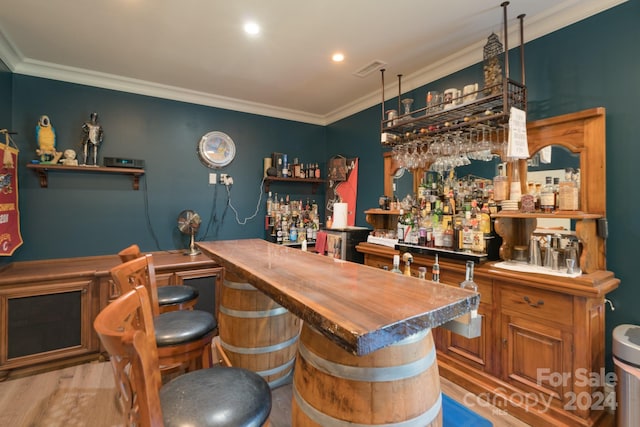 bar with light hardwood / wood-style flooring, ornamental molding, and butcher block counters