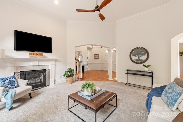 living room with a towering ceiling, decorative columns, light carpet, ceiling fan, and crown molding