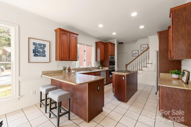 kitchen with kitchen peninsula, crown molding, light stone countertops, a center island, and a kitchen bar