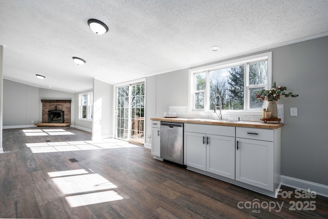 kitchen with tasteful backsplash, stainless steel dishwasher, vaulted ceiling, sink, and white cabinets