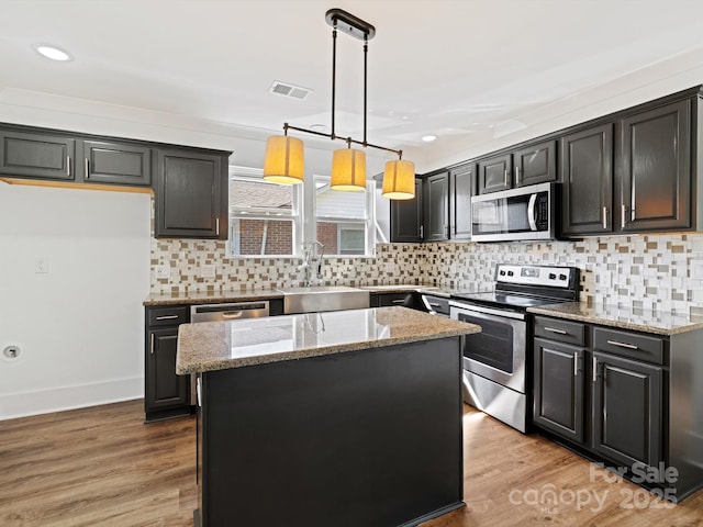 kitchen featuring sink, light hardwood / wood-style flooring, light stone countertops, appliances with stainless steel finishes, and a kitchen island