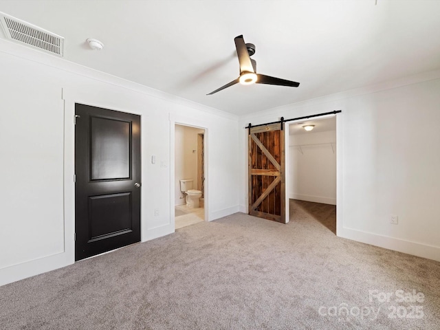 unfurnished bedroom featuring a spacious closet, ceiling fan, a barn door, light carpet, and a closet