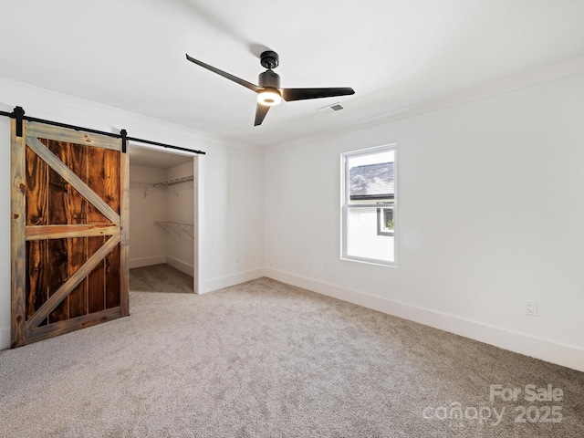 unfurnished bedroom with light carpet, ceiling fan, a barn door, a spacious closet, and a closet