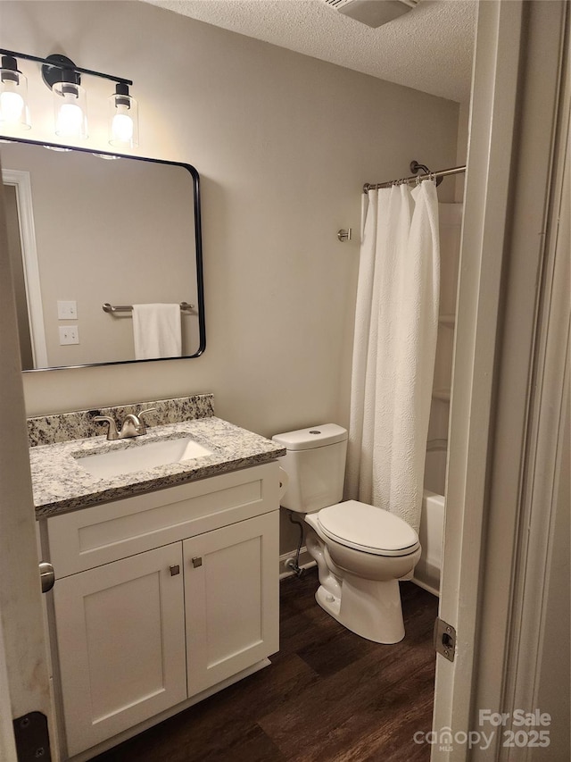 full bathroom with hardwood / wood-style floors, vanity, shower / bath combination with curtain, a textured ceiling, and toilet