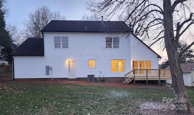 back house at dusk featuring a deck, a lawn, and central air condition unit