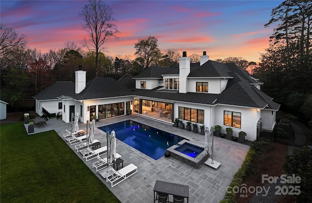 back house at dusk with a patio area, a pool with hot tub, and a lawn