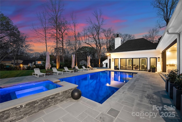 pool at dusk with an in ground hot tub and a patio area