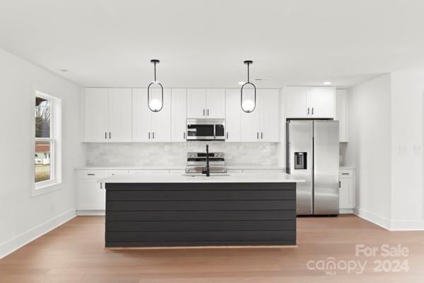 kitchen with sink, stainless steel appliances, decorative light fixtures, white cabinets, and light wood-type flooring