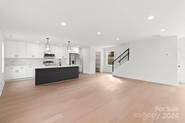 kitchen with a center island with sink, white cabinets, light wood-type flooring, and stainless steel appliances