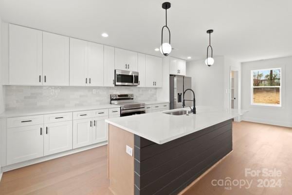 kitchen featuring hanging light fixtures, white cabinets, stainless steel appliances, and a center island with sink