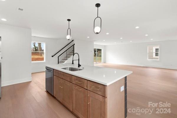 kitchen featuring dishwasher, sink, hanging light fixtures, light hardwood / wood-style flooring, and an island with sink