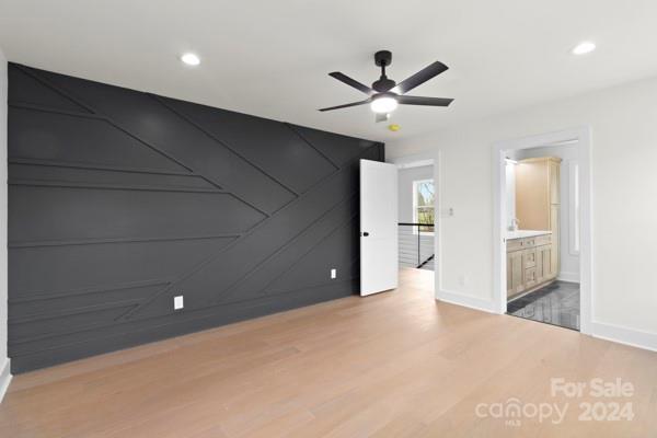 unfurnished bedroom featuring hardwood / wood-style flooring, ensuite bath, and ceiling fan