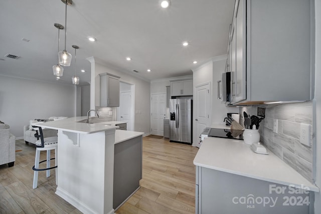 kitchen with a breakfast bar, stainless steel appliances, hanging light fixtures, and light hardwood / wood-style floors