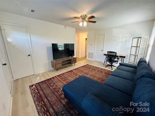 living room with a textured ceiling, ceiling fan, and light hardwood / wood-style floors