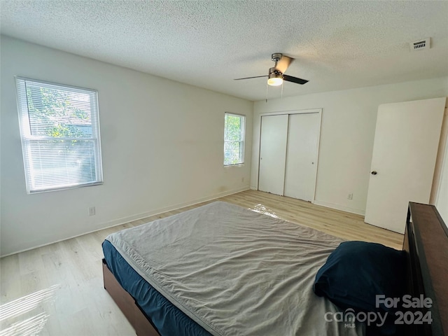 bedroom featuring light wood-type flooring, a textured ceiling, ceiling fan, and a closet