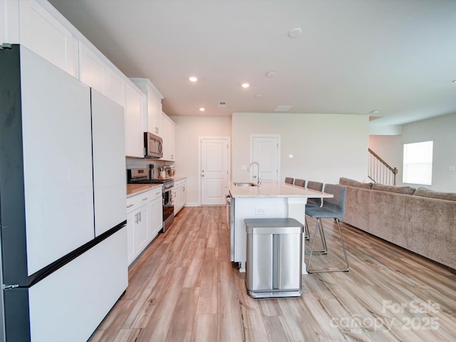 kitchen with a kitchen island with sink, a breakfast bar area, stainless steel appliances, sink, and white cabinetry