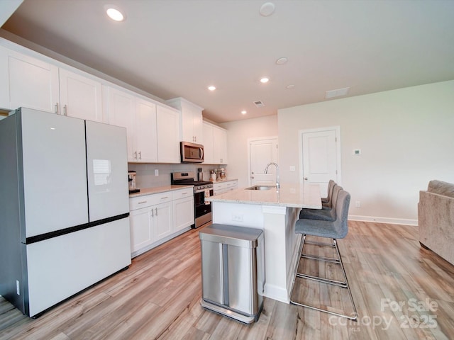 kitchen featuring stainless steel appliances, an island with sink, light hardwood / wood-style floors, white cabinetry, and sink