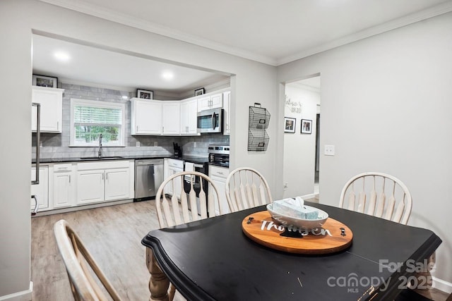 dining room with ornamental molding, sink, and light hardwood / wood-style flooring