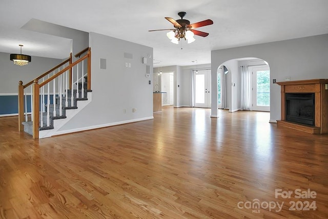 unfurnished living room with ceiling fan with notable chandelier and light wood-type flooring