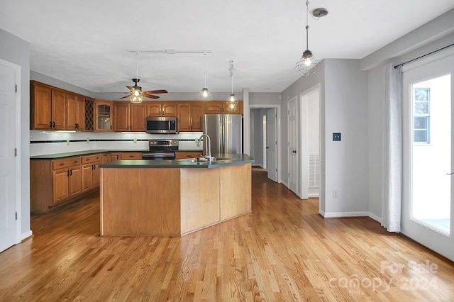 kitchen featuring appliances with stainless steel finishes, light hardwood / wood-style floors, a kitchen island with sink, and ceiling fan