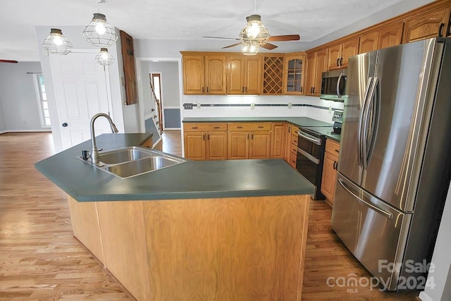 kitchen with light hardwood / wood-style floors, stainless steel appliances, ceiling fan, a center island with sink, and sink