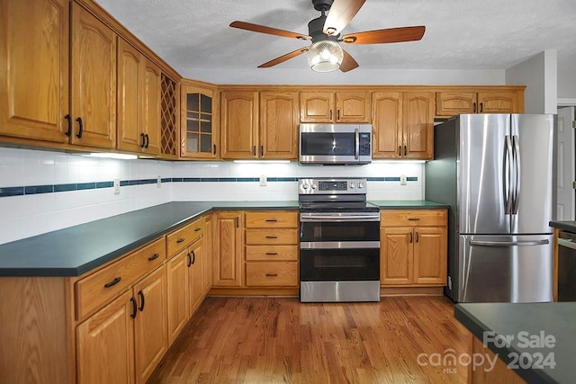 kitchen with a textured ceiling, hardwood / wood-style flooring, stainless steel appliances, backsplash, and ceiling fan