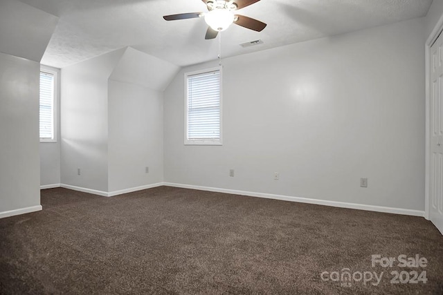 additional living space with ceiling fan, lofted ceiling, dark carpet, and a healthy amount of sunlight