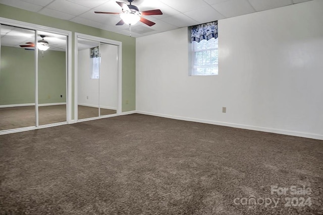 unfurnished bedroom with a paneled ceiling, dark carpet, ceiling fan, and multiple closets