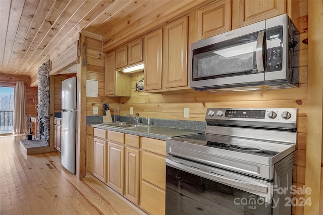 kitchen with sink, wooden walls, light wood-type flooring, light brown cabinetry, and appliances with stainless steel finishes