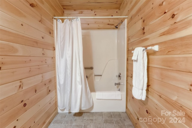 bathroom with wooden ceiling, shower / tub combo with curtain, and wooden walls