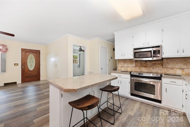 kitchen featuring a breakfast bar, stainless steel appliances, a center island, ceiling fan, and hardwood / wood-style floors